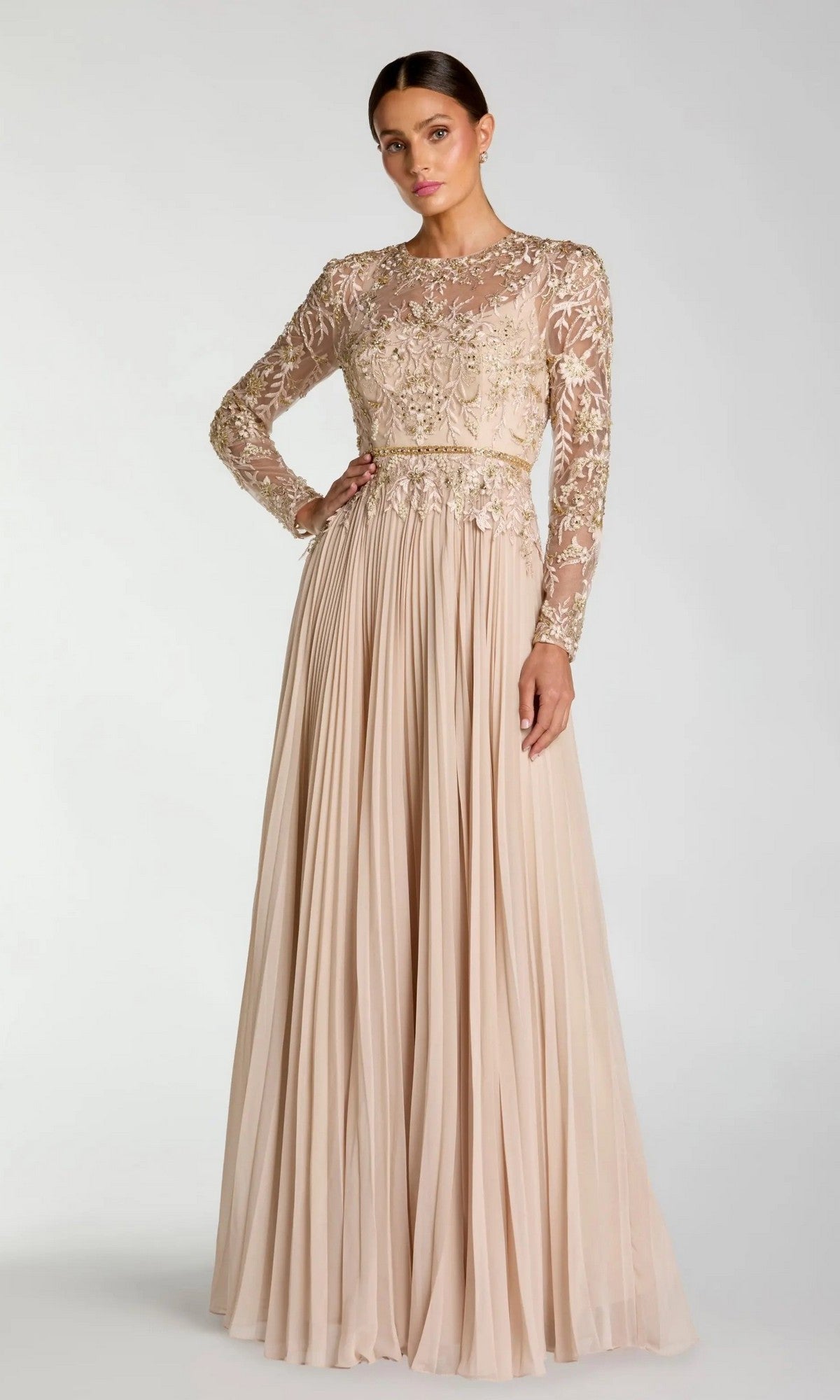A woman models the Mac Duggal 11986 long formal dress in taupe, featuring intricate bodice embroidery and sheer long sleeves, standing against a plain light background to highlight this refined, modest evening gown.